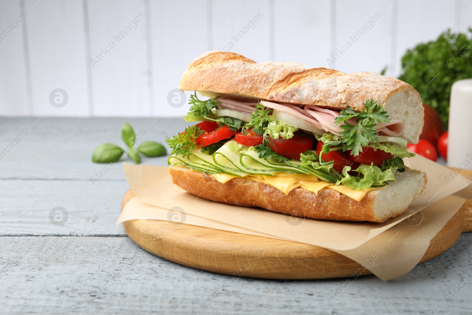 Tasty baguette sandwich with ham, cheese and vegetables on wooden table against grey background, closeup Photo of Tasty baguette sandwich with ham, cheese and vegetables on wooden table against grey background, closeup
