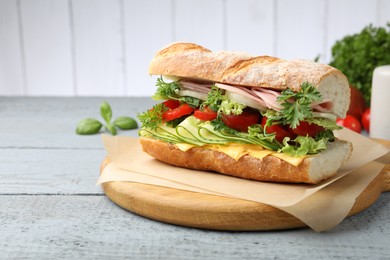 Photo of Tasty baguette sandwich with ham, cheese and vegetables on wooden table against grey background, closeup