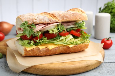 Photo of Tasty baguette sandwich with ham, cheese and vegetables on wooden table against grey background, closeup
