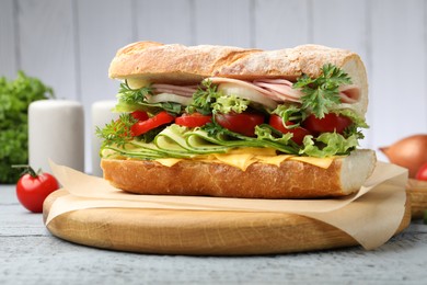 Photo of Tasty baguette sandwich with ham, cheese and vegetables on grey wooden table, closeup