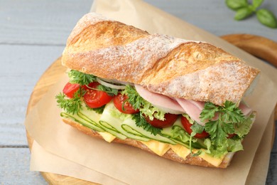 Photo of Tasty baguette sandwich with ham, cheese and vegetables on grey wooden table, closeup