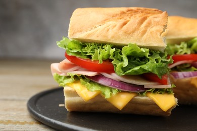Photo of Pieces of tasty baguette sandwich with ham, cheese and vegetables on wooden table against grey background, closeup