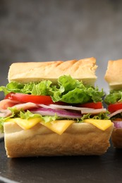 Photo of Piece of tasty baguette sandwich with ham, cheese and vegetables on black board against grey background, closeup