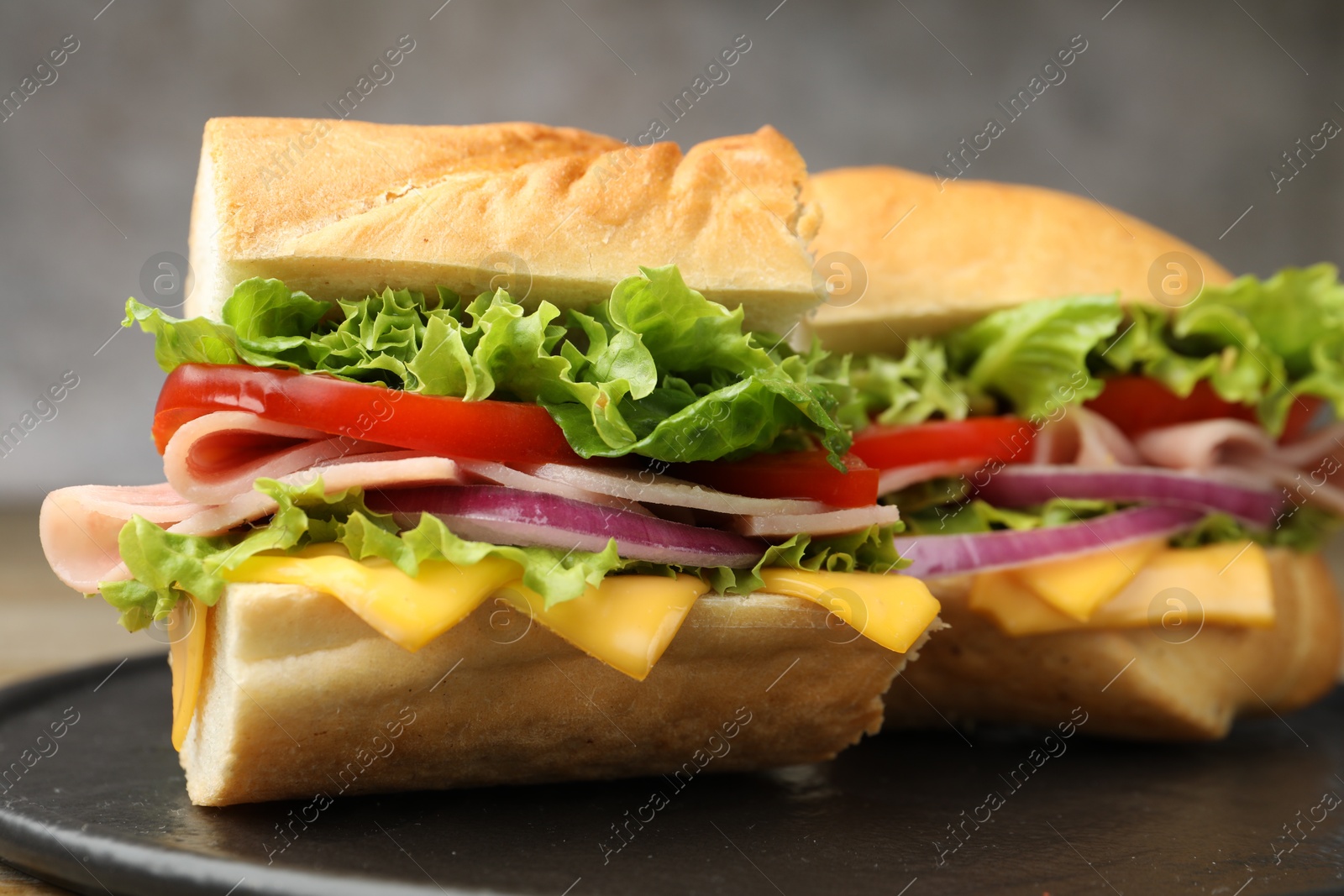 Pieces of tasty baguette sandwich with ham, cheese and vegetables on table against grey background, closeup Photo of Pieces of tasty baguette sandwich with ham, cheese and vegetables on table against grey background, closeup