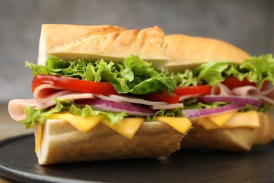 Photo of Pieces of tasty baguette sandwich with ham, cheese and vegetables on table against grey background, closeup