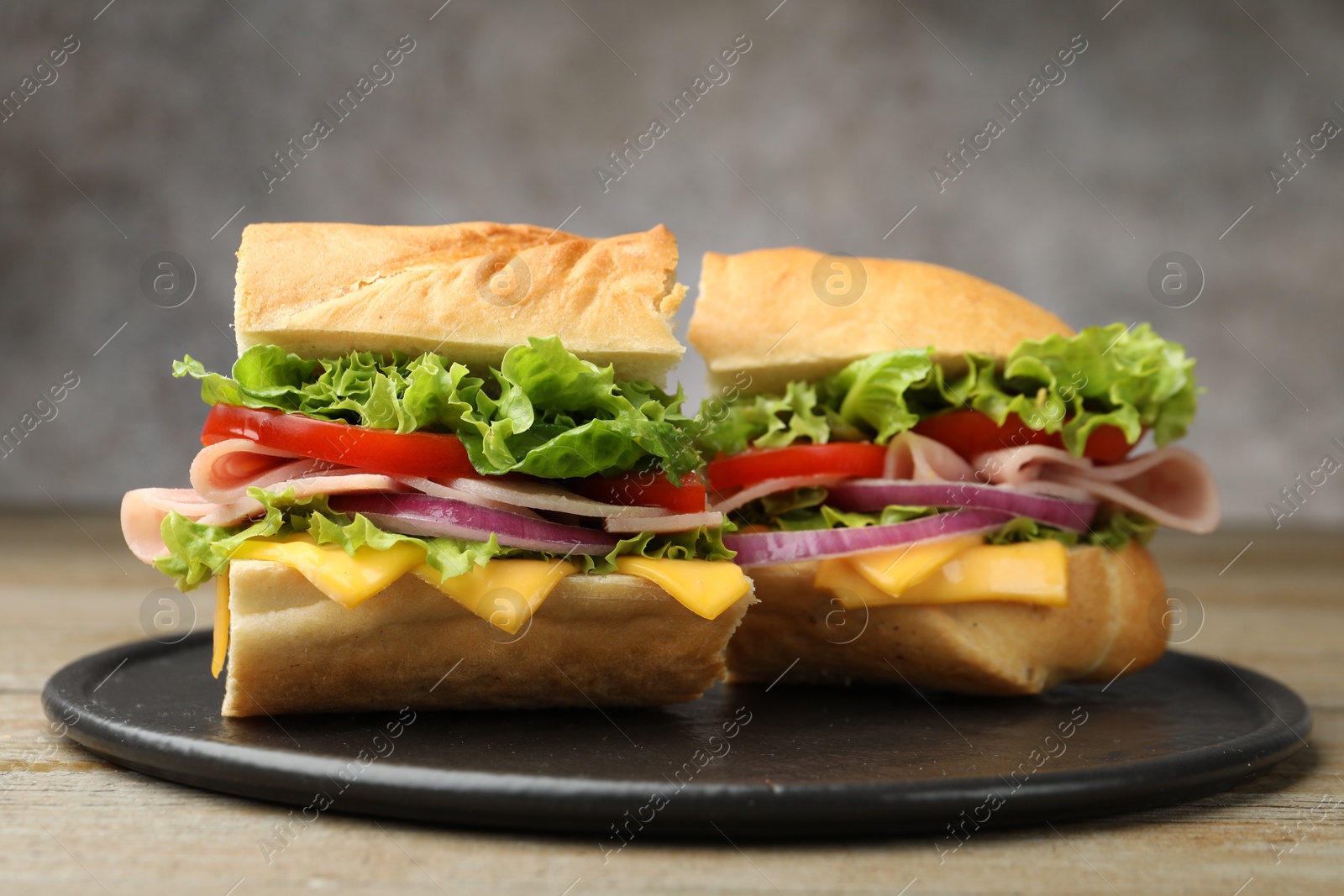 Pieces of tasty baguette sandwich with ham, cheese and vegetables on wooden table against grey background, closeup Photo of Pieces of tasty baguette sandwich with ham, cheese and vegetables on wooden table against grey background, closeup