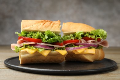 Photo of Pieces of tasty baguette sandwich with ham, cheese and vegetables on wooden table against grey background, closeup