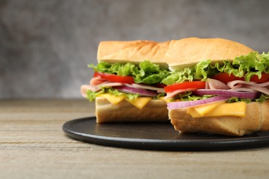 Photo of Pieces of tasty baguette sandwich with ham, cheese and vegetables on wooden table against grey background, closeup