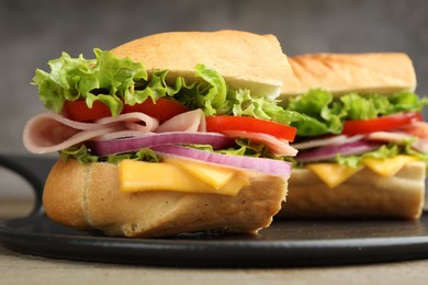 Photo of Pieces of tasty baguette sandwich with ham, cheese and vegetables on table against grey background, closeup