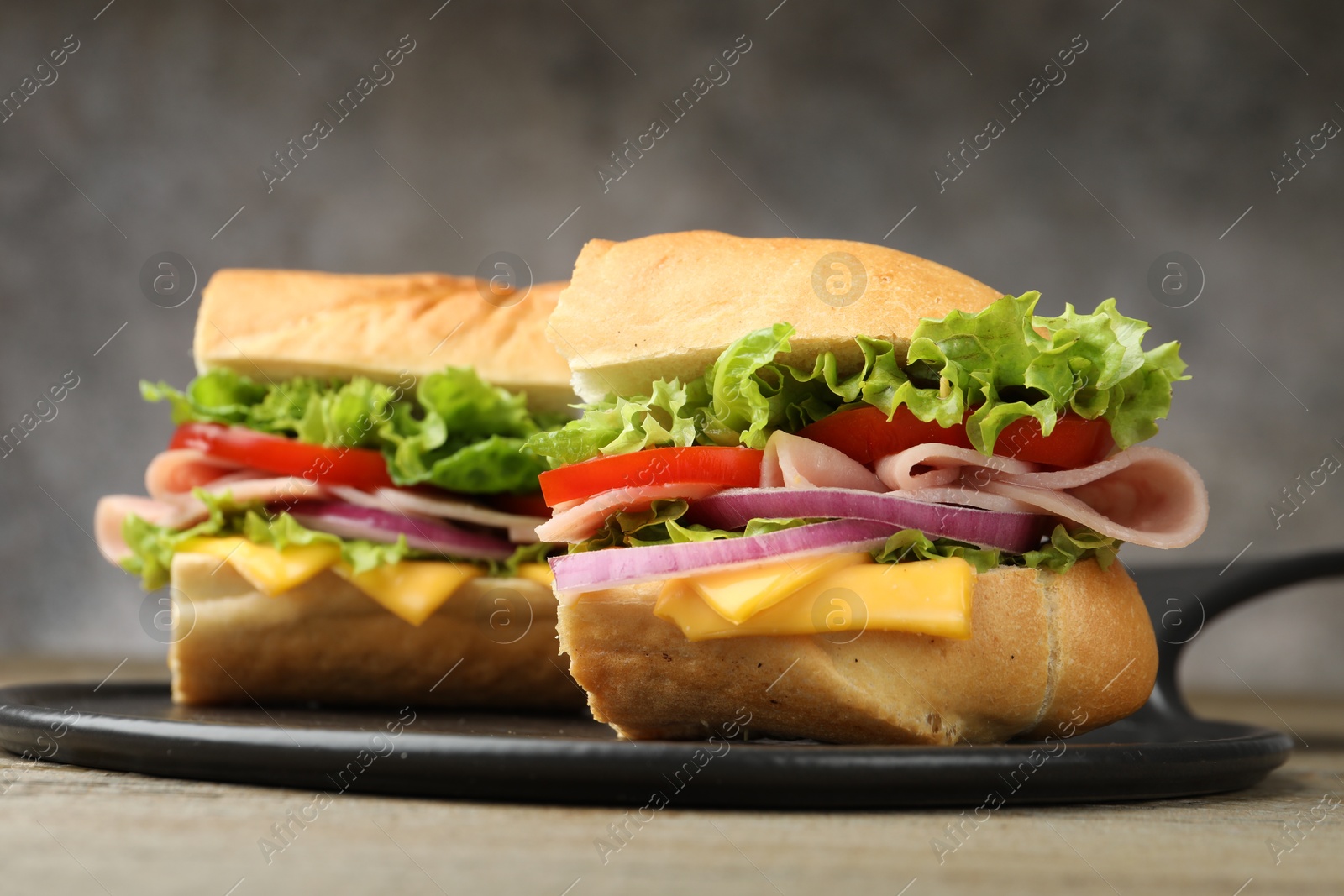 Photo of Pieces of tasty baguette sandwich with ham, cheese and vegetables on table against grey background, closeup