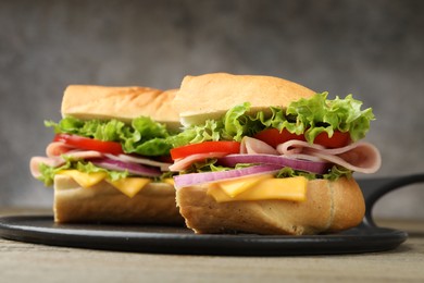 Photo of Pieces of tasty baguette sandwich with ham, cheese and vegetables on table against grey background, closeup