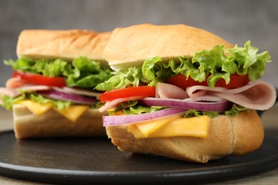 Photo of Pieces of tasty baguette sandwich with ham, cheese and vegetables on wooden table against grey background, closeup