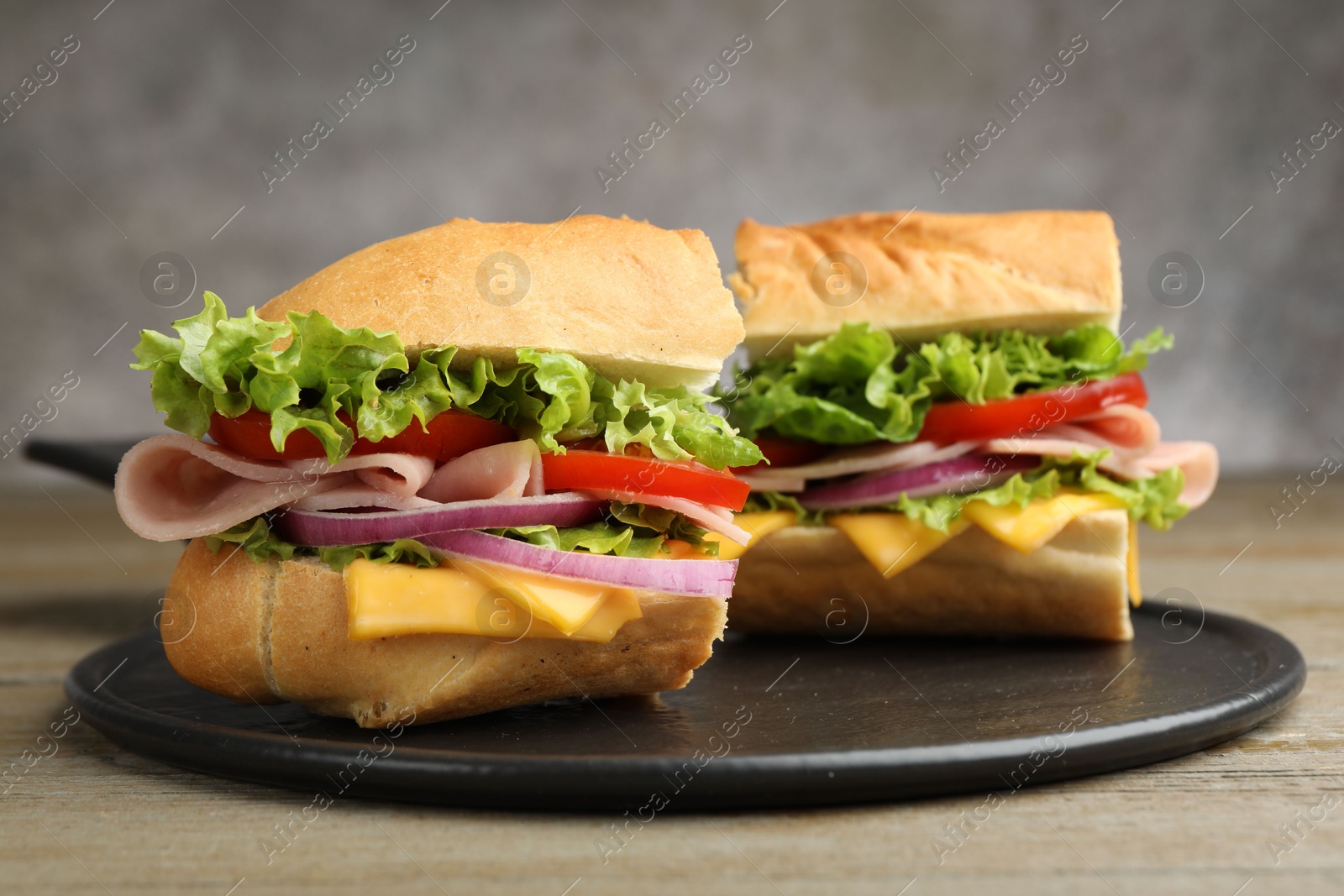 Photo of Pieces of tasty baguette sandwich with ham, cheese and vegetables on wooden table against grey background, closeup