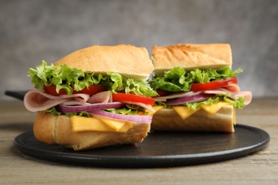 Photo of Pieces of tasty baguette sandwich with ham, cheese and vegetables on wooden table against grey background, closeup