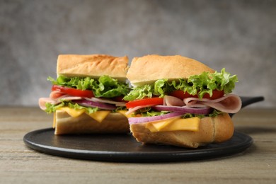 Photo of Pieces of tasty baguette sandwich with ham, cheese and vegetables on wooden table against grey background, closeup
