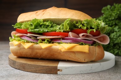 Photo of Tasty baguette sandwich with ham, cheese and vegetables on grey textured table against blurred brown background, closeup