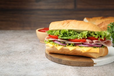 Photo of Tasty baguette sandwich with ham, cheese and vegetables on grey textured table against wooden background, closeup. Space for text