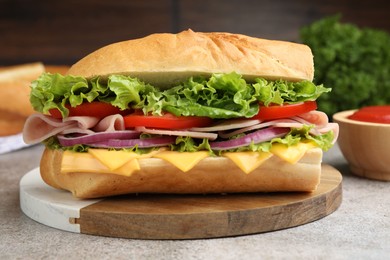 Photo of Tasty baguette sandwich with ham, cheese and vegetables on grey textured table against blurred brown background, closeup