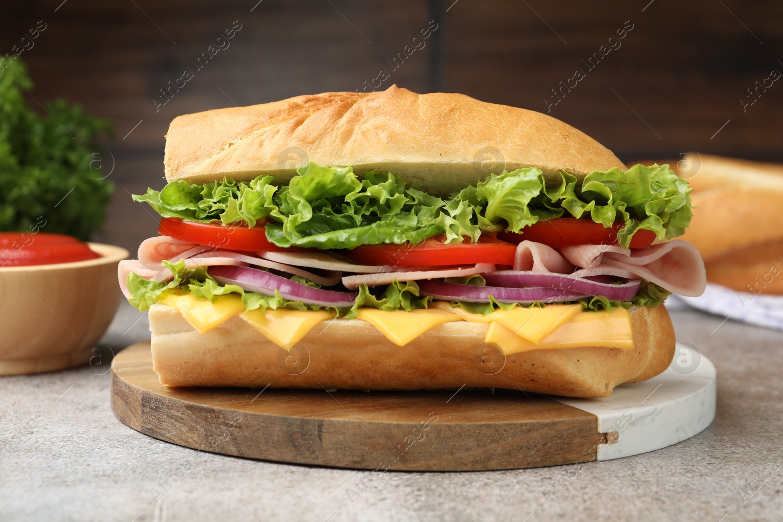 Tasty baguette sandwich with ham, cheese and vegetables on grey textured table against blurred brown background, closeup Photo of Tasty baguette sandwich with ham, cheese and vegetables on grey textured table against blurred brown background, closeup