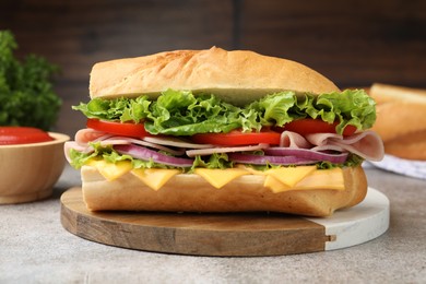 Photo of Tasty baguette sandwich with ham, cheese and vegetables on grey textured table against blurred brown background, closeup