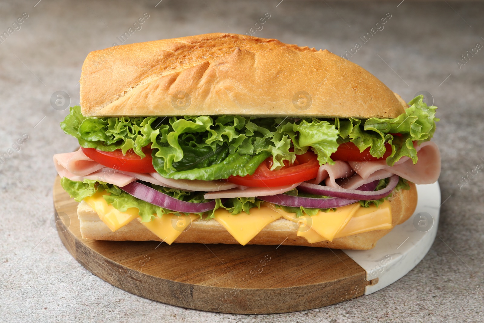 Tasty baguette sandwich with ham, cheese and vegetables on grey textured table, closeup Photo of Tasty baguette sandwich with ham, cheese and vegetables on grey textured table, closeup