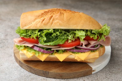Photo of Tasty baguette sandwich with ham, cheese and vegetables on grey textured table, closeup