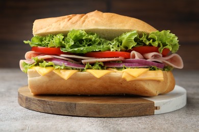 Photo of Tasty baguette sandwich with ham, cheese and vegetables on grey textured table against blurred brown background, closeup