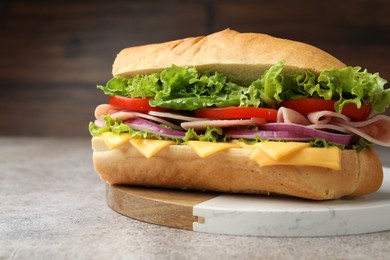 Photo of Tasty baguette sandwich with ham, cheese and vegetables on grey textured table against blurred brown background, closeup