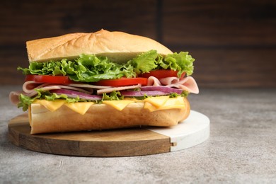 Photo of Tasty baguette sandwich with ham, cheese and vegetables on grey textured table against blurred brown background, closeup