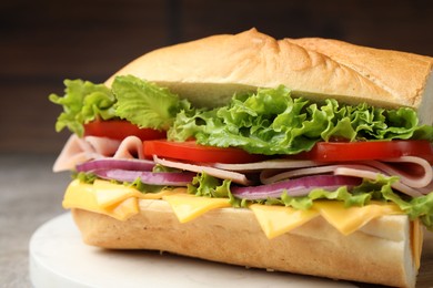 Photo of Tasty baguette sandwich with ham, cheese and vegetables on grey table against blurred brown background, closeup