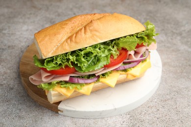 Photo of Tasty baguette sandwich with ham, cheese and vegetables on grey textured table, closeup