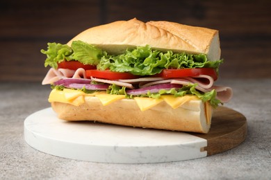 Photo of Tasty baguette sandwich with ham, cheese and vegetables on grey textured table against blurred brown background, closeup
