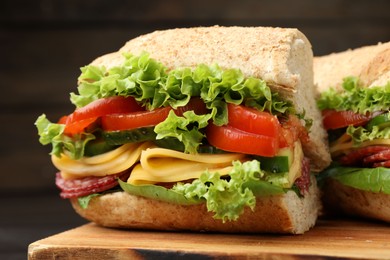 Photo of Pieces of tasty baguette sandwich with smoked sausage, cheese and vegetables on wooden board against dark background, closeup