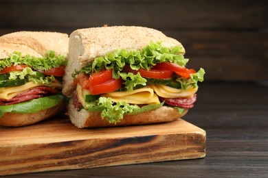 Photo of Pieces of tasty baguette sandwich with smoked sausage, cheese and vegetables on wooden table, closeup