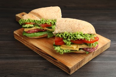Photo of Pieces of tasty baguette sandwich with smoked sausage, cheese and vegetables on wooden table, closeup