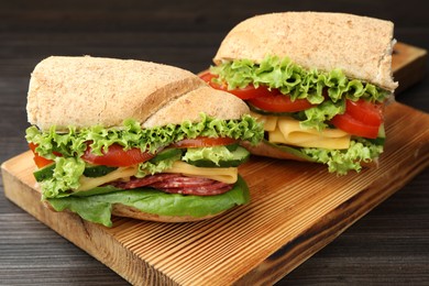 Photo of Pieces of tasty baguette sandwich with smoked sausage, cheese and vegetables on wooden table, closeup