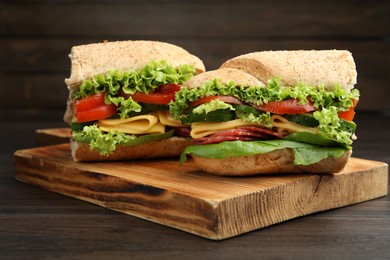 Photo of Pieces of tasty baguette sandwich with smoked sausage, cheese and vegetables on wooden table, closeup