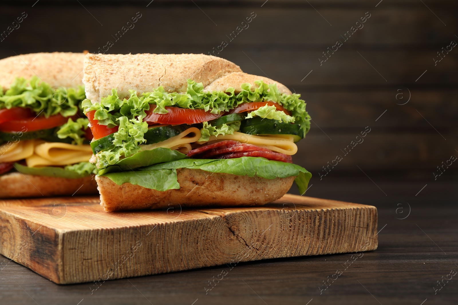 Pieces of tasty baguette sandwich with smoked sausage, cheese and vegetables on wooden table, closeup Photo of Pieces of tasty baguette sandwich with smoked sausage, cheese and vegetables on wooden table, closeup