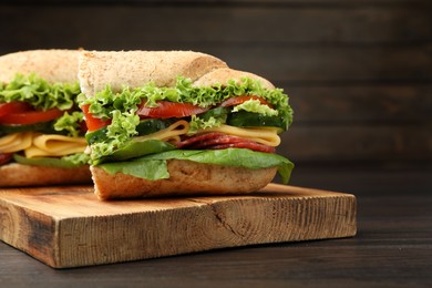 Photo of Pieces of tasty baguette sandwich with smoked sausage, cheese and vegetables on wooden table, closeup