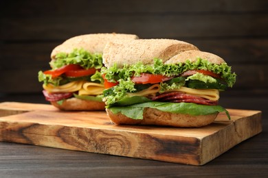 Photo of Pieces of tasty baguette sandwich with smoked sausage, cheese and vegetables on wooden table, closeup