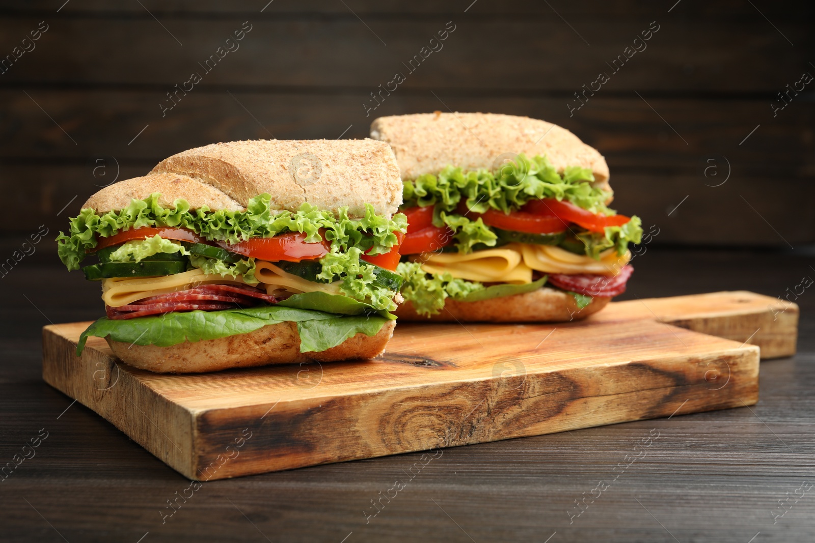 Photo of Pieces of tasty baguette sandwich with smoked sausage, cheese and vegetables on wooden table, closeup