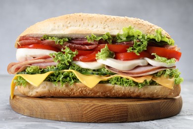 Photo of Tasty baguette sandwich with ham, cheese and vegetables on grey textured table, closeup
