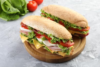 Photo of Tasty baguette sandwiches with ham, cheese and vegetables on grey textured table, closeup