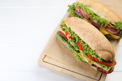 Photo of Tasty baguette sandwiches with smoked sausage, cheese and vegetables on white wooden table, closeup. Space for text