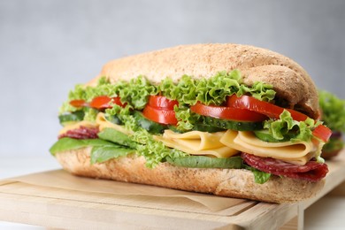 Photo of Tasty baguette sandwich with smoked sausage, cheese and vegetables on white table, closeup