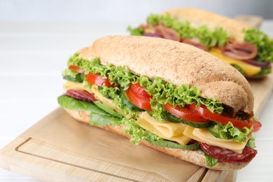Photo of Tasty baguette sandwiches with smoked sausage, cheese and vegetables on white table, closeup