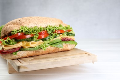 Photo of Tasty baguette sandwich with smoked sausage, cheese and vegetables on white wooden table, closeup