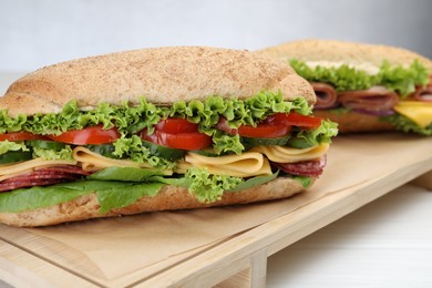 Photo of Tasty baguette sandwiches with smoked sausage, cheese and vegetables on white wooden table against grey background, closeup