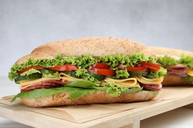 Photo of Tasty baguette sandwiches with smoked sausage, cheese and vegetables on white wooden table against grey background, closeup
