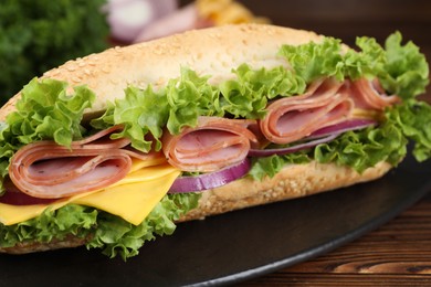 Photo of Tasty baguette sandwich with ham, cheese and vegetables on wooden table, closeup
